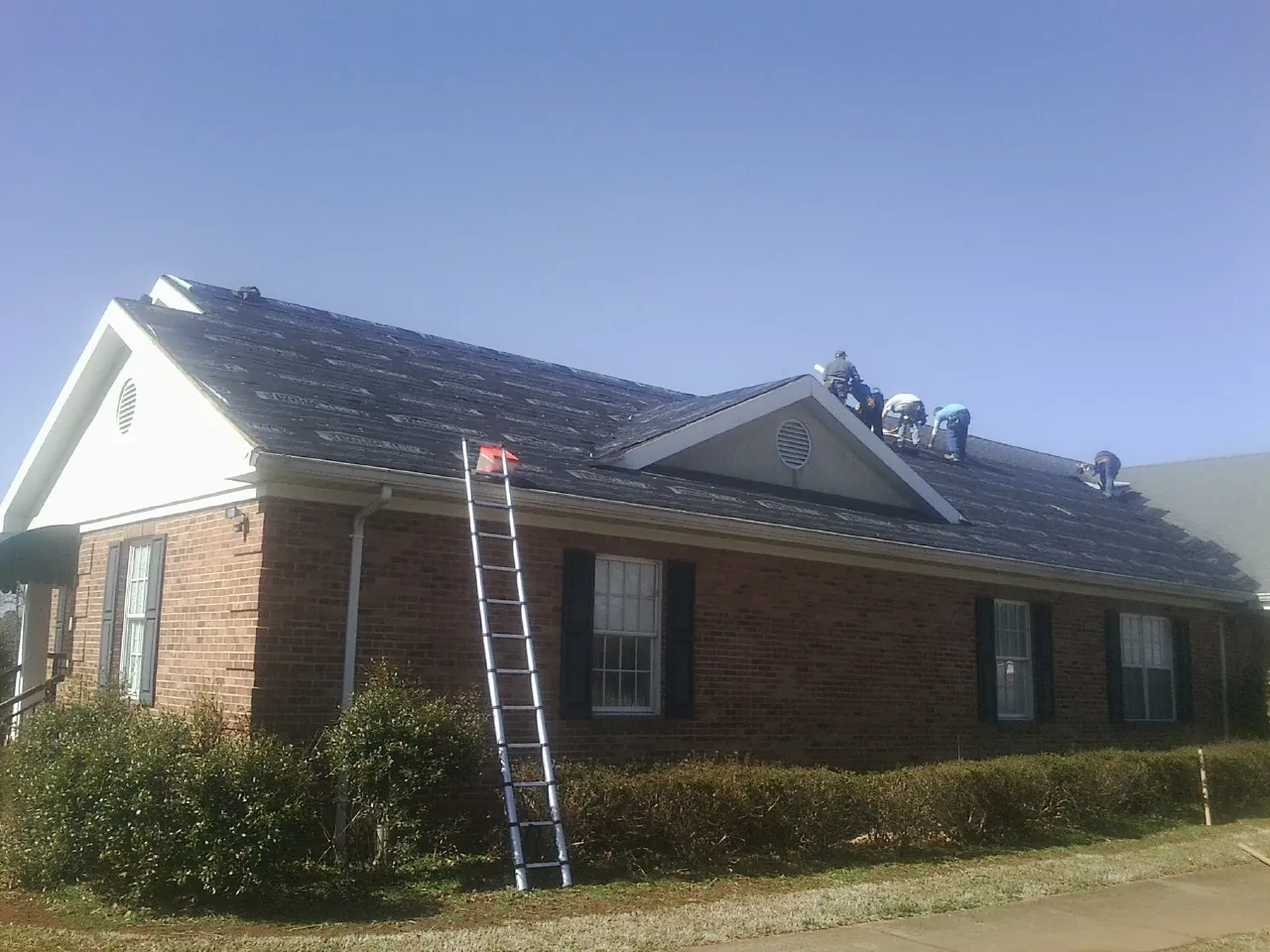 Crew tearing shingles off a brick ranch roof with a ladder set — Metal Roof Repair work by our crew in Whitesburg