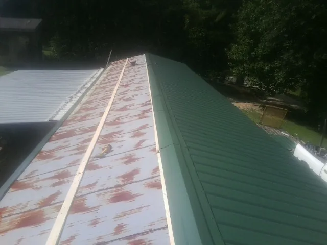 Old rusted panels beside newly installed green metal roofing — Wind Damage Roof Repair by Roofing Brothers in Whitesburg