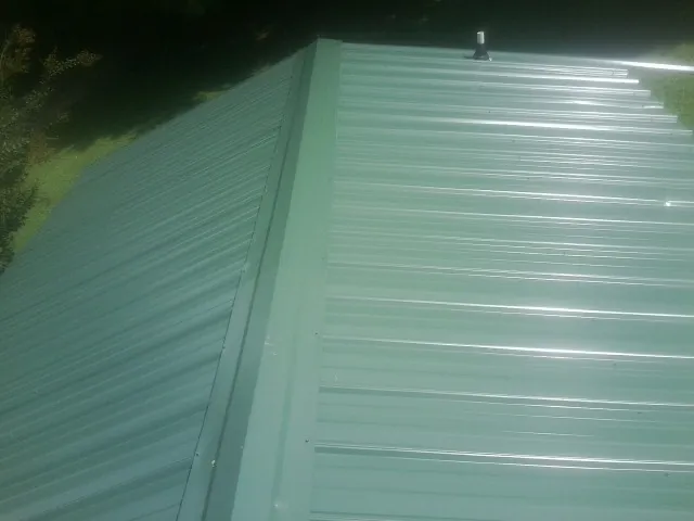 New green metal panels meeting at the ridge of a roof — Flat Roof Repair work by our crew in Whitesburg
