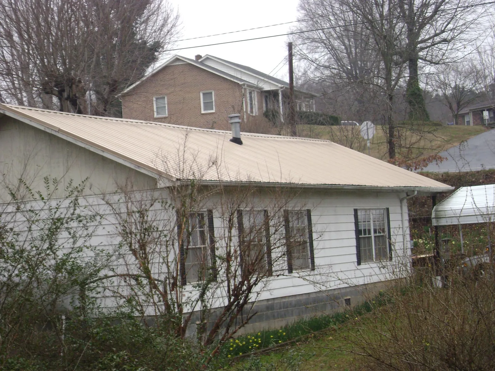 Tan metal roof on a white sided house set into a hillside — Commercial Roofing by Roofing Brothers in Whitesburg
