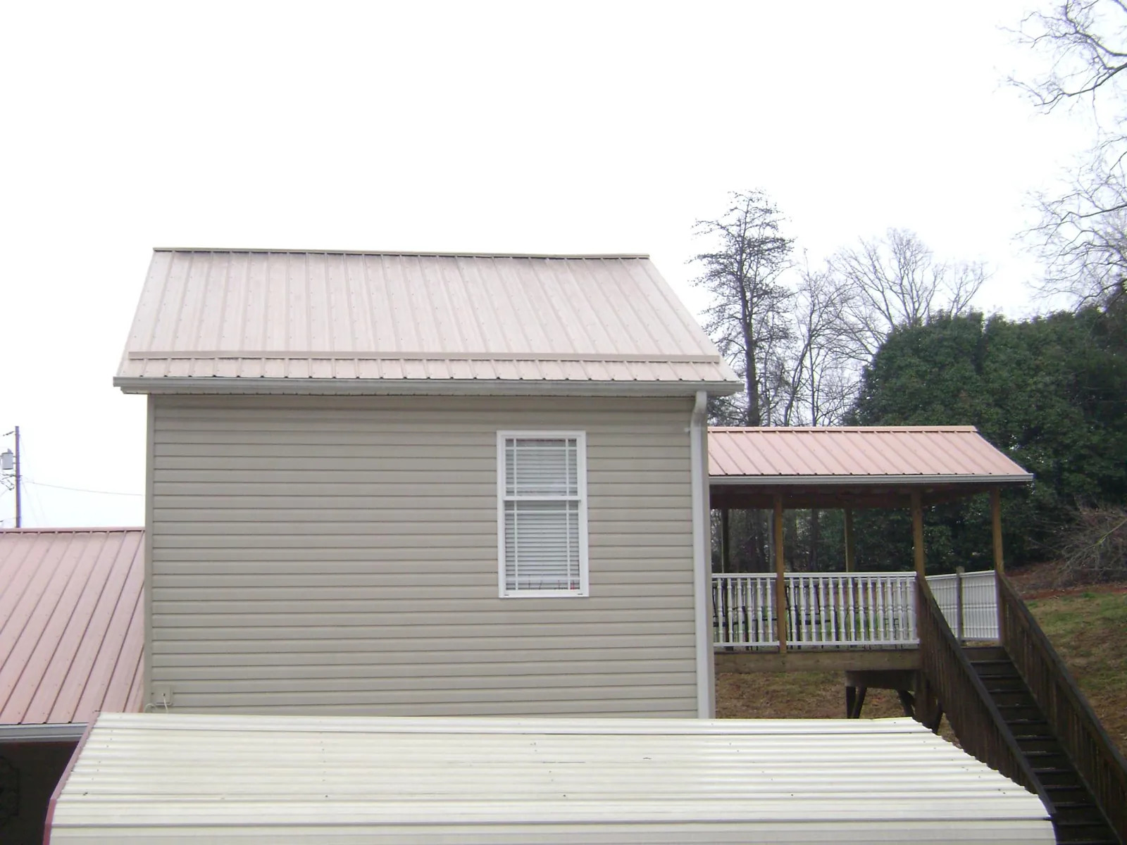 Tan metal roofs on a two story addition and attached porch, from a Roof Replacement job in Whitesburg